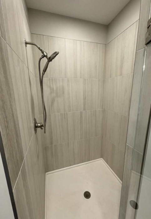 A modern custom shower stall in Manhattan, KS, with light gray vertically striped tiles and a white hexagonal base with a drain.